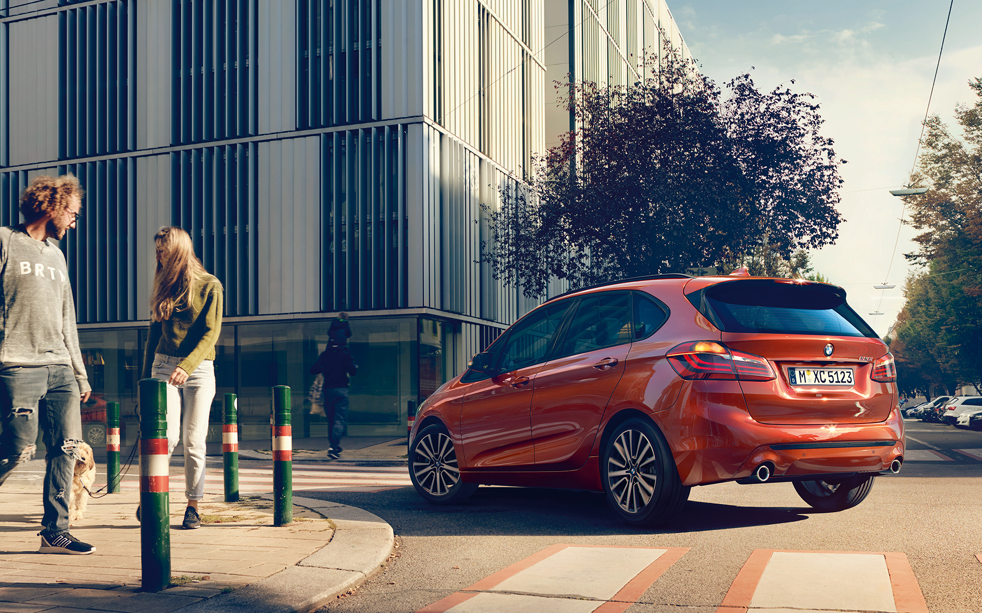 Orangener BMW 2er Active Tourer biegt in der Stadt in eine Straße ein Orangener BMW 2er Active Tourer biegt in der Stadt in eine Straße ein