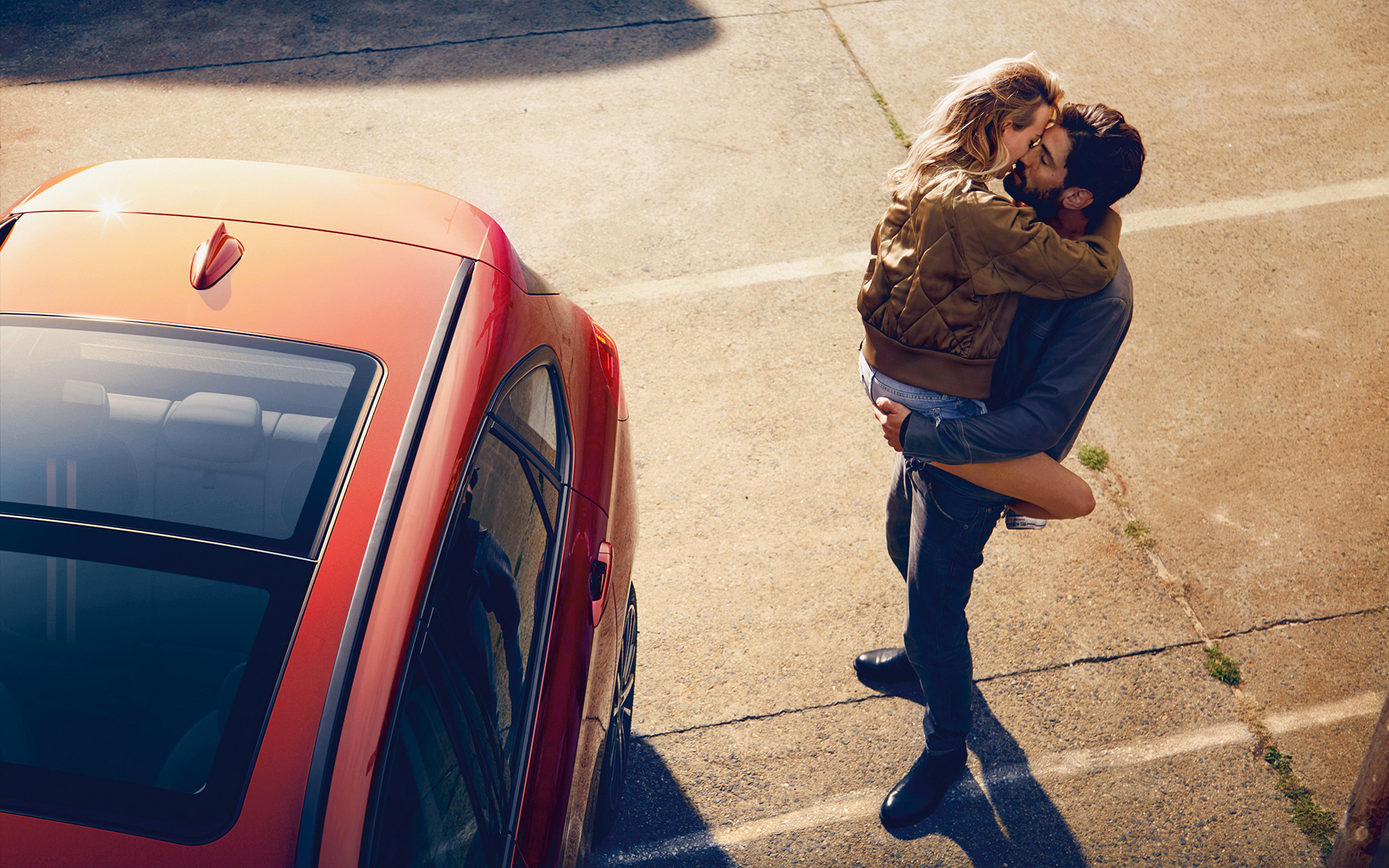 Ein Paar küsst sich neben einem orangenen BMW 2er Active Tourer Ein Paar küsst sich neben einem orangenen BMW 2er Active Tourer