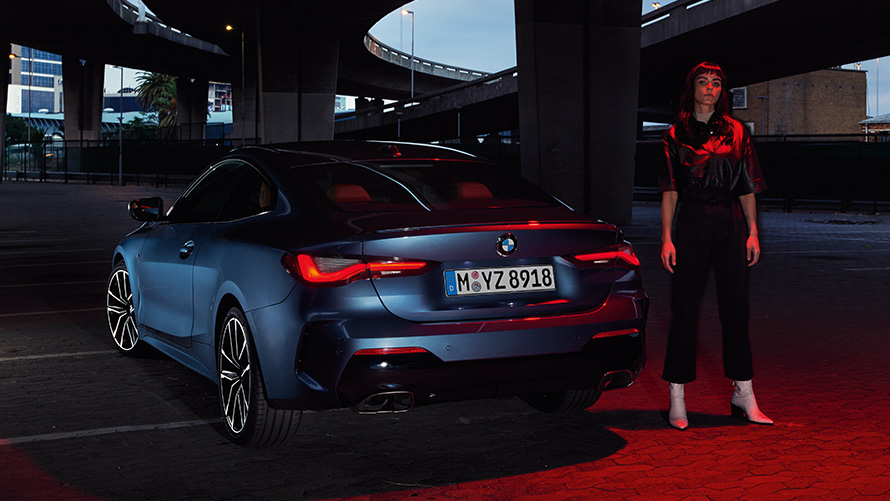 BMW 4er Coupé (G22), Artic Race Blue metallic, Heckansicht mit Person BMW 4er Coupé (G22), Artic Race Blue metallic, Heckansicht mit Person