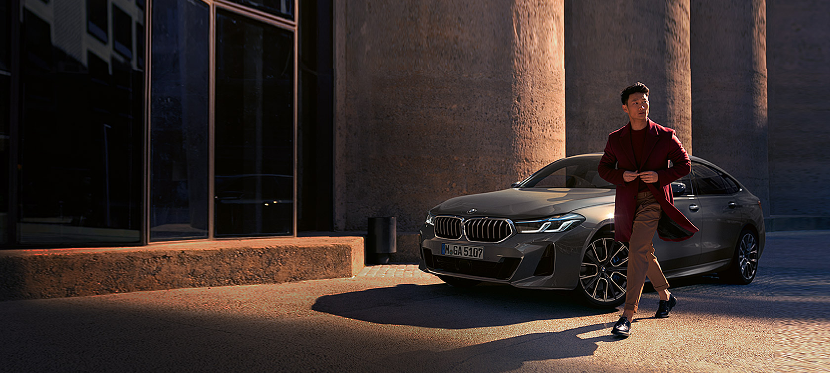 BMW 6er Gran Turismo 640i xDrive G32 2020 Berninagrau, Mann vor BMW in Dreiviertel-Heckansicht stehend