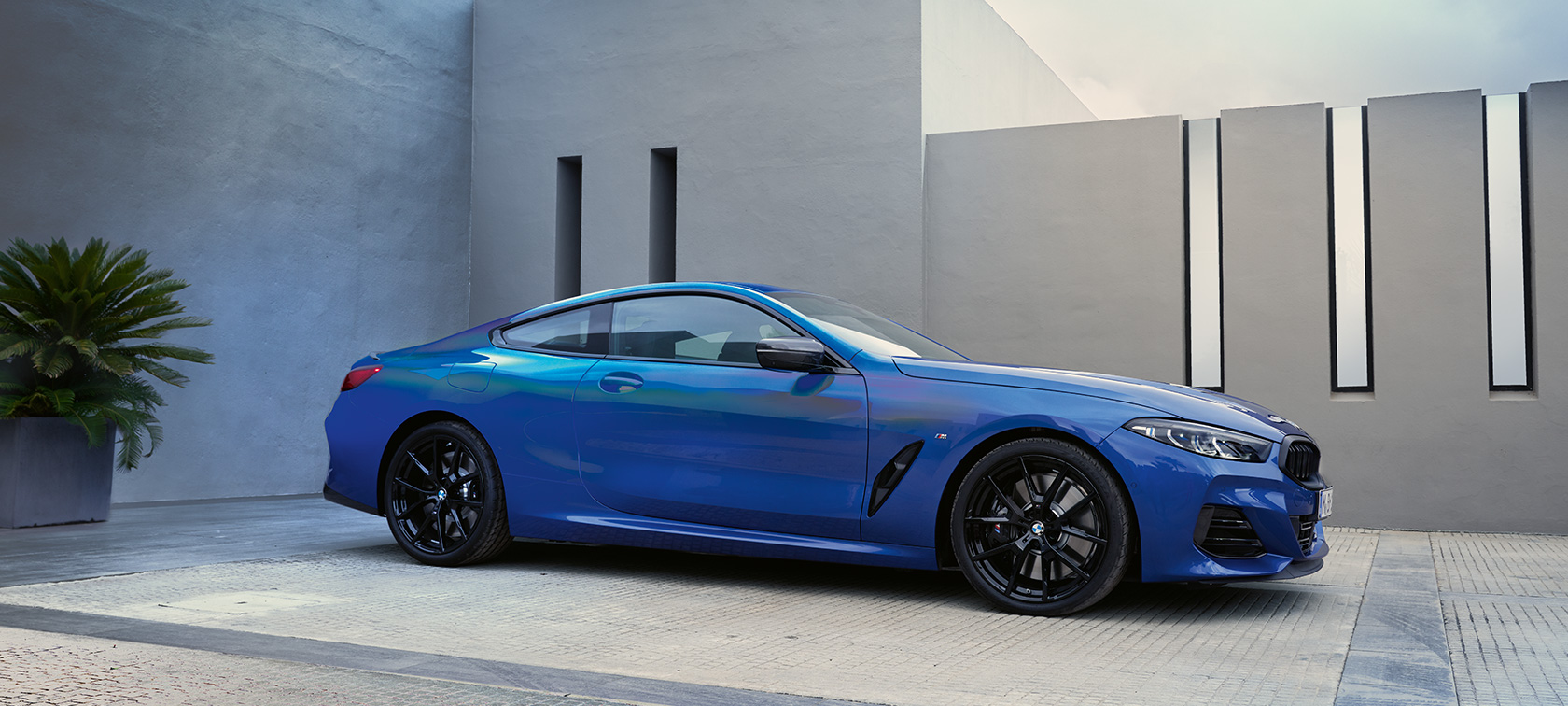 BMW 8er Coupé G15 LCI Facelift 2022 M Portimao Blau metallic Seitenansicht stehend vor Hauswand 
