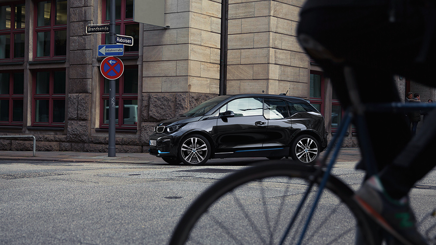 BMW i3s I01 2018 Fluid Black mit Akzent BMW i Blau Seitenansicht in urbaner Kulisse fahrend