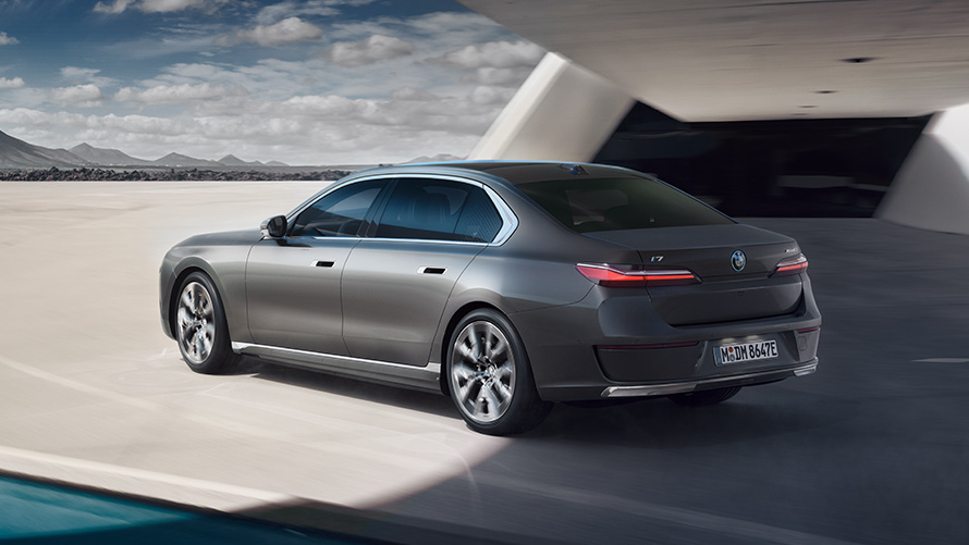 BMW i7 Limousine G70 3/4 Heckansicht BMW i7 Limousine G70 Oxidgrau metallic 3/4 Heckansicht stehend vor Gebäude