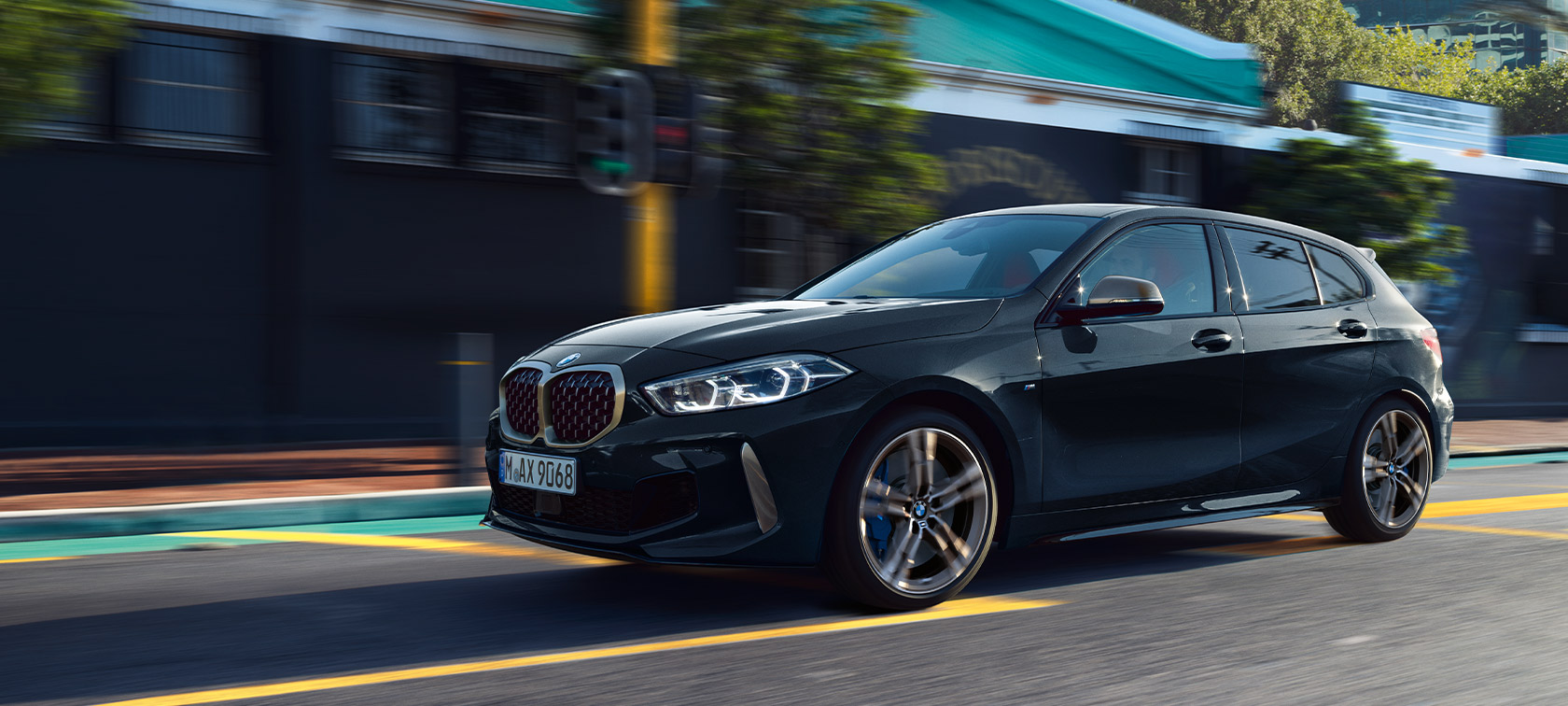 BMW M135i xDrive (F40) in Saphirschwarz metallic fahrendes Auto in urbaner Umgebung