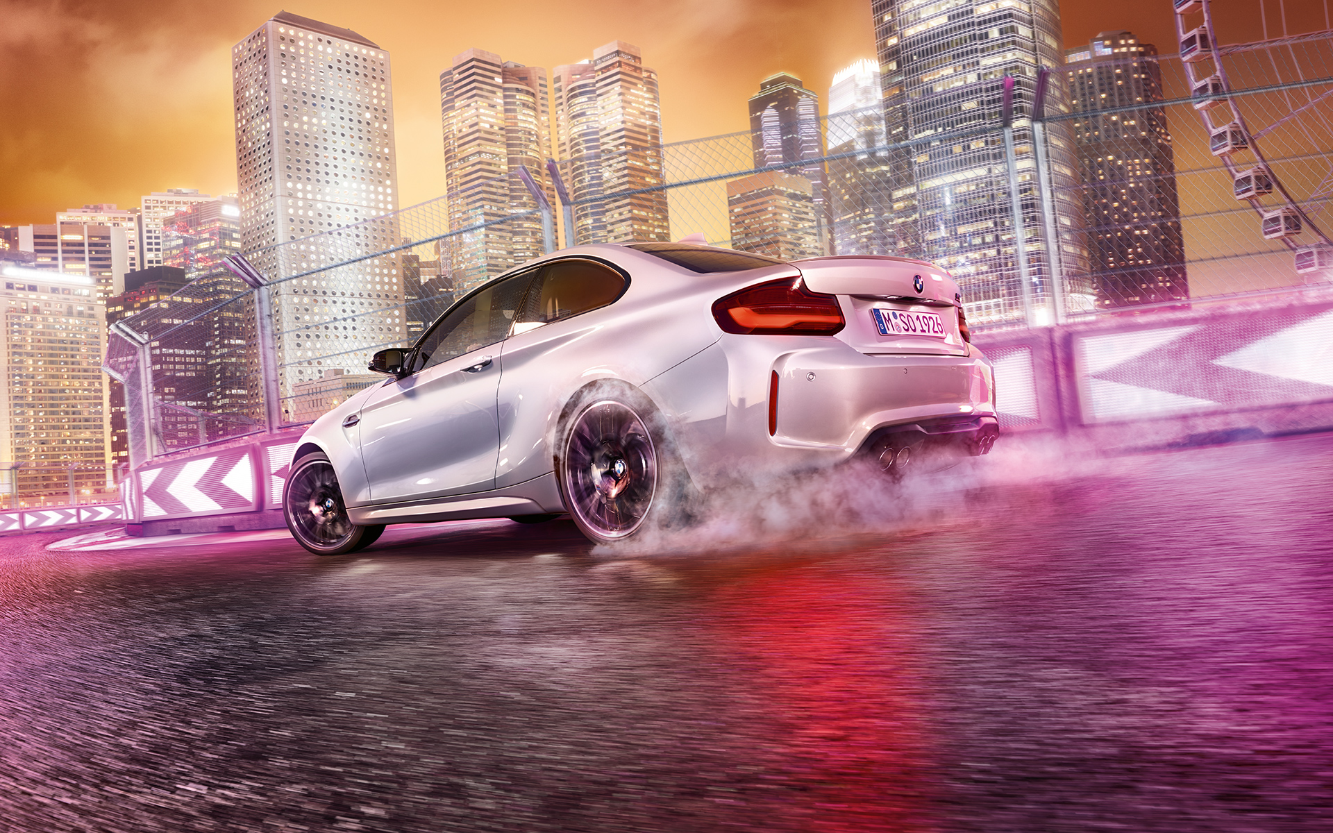 BMW M2 Competition gibt Gas Weißer BMW M2 Competition driftet auf Rennstrecke vor nächtlicher Skyline.