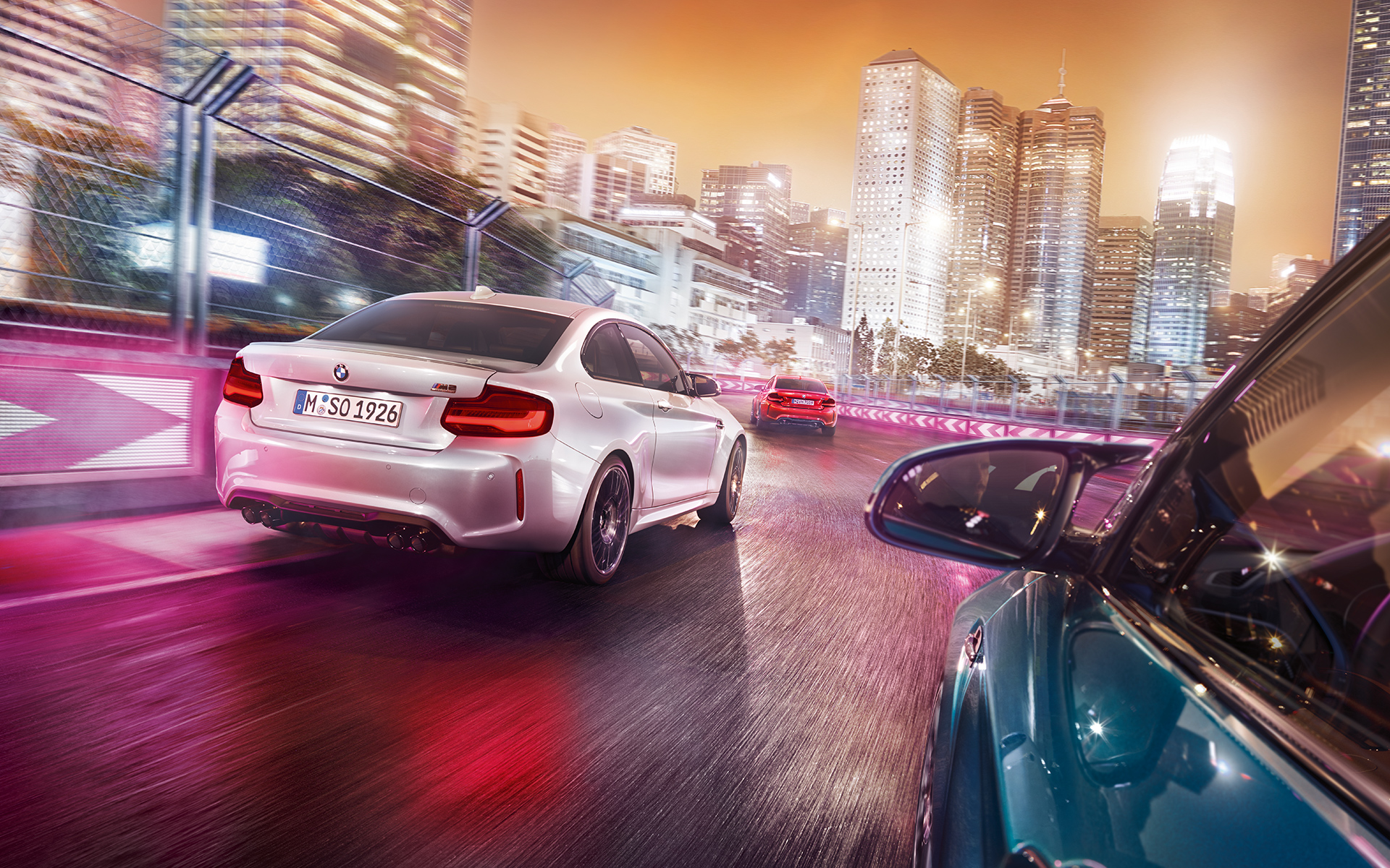 BMW M2 Competition Rückansicht Drei BMW M2 Competition in der Rückansicht fahren auf Rennstrecke vor beleuchteter Skyline .
