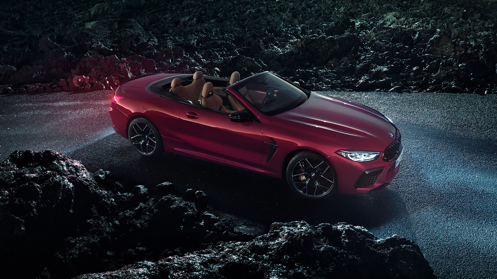 BMW M8 Competition Cabriolet, Dreiviertel-Seitenansicht. BMW M8 Competition Cabriolet in Motegi Rot metallic mit geöffnetem Verdeck, Dreiviertel-Seitenansicht, stehend bei Nacht auf Asphalt.