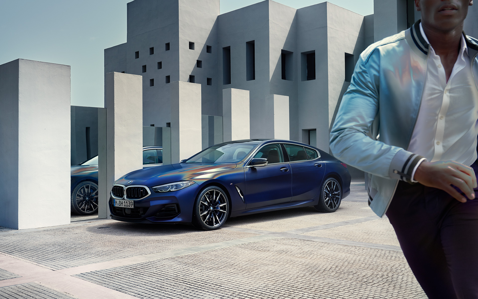 BMW M850i xDrive Gran Coupé G16 LCI Facelift 2022 BMW Individual Frozen Tansanitblau metallic Dreiviertel-Frontansicht stehend mit männlichem Model im Vordergrund