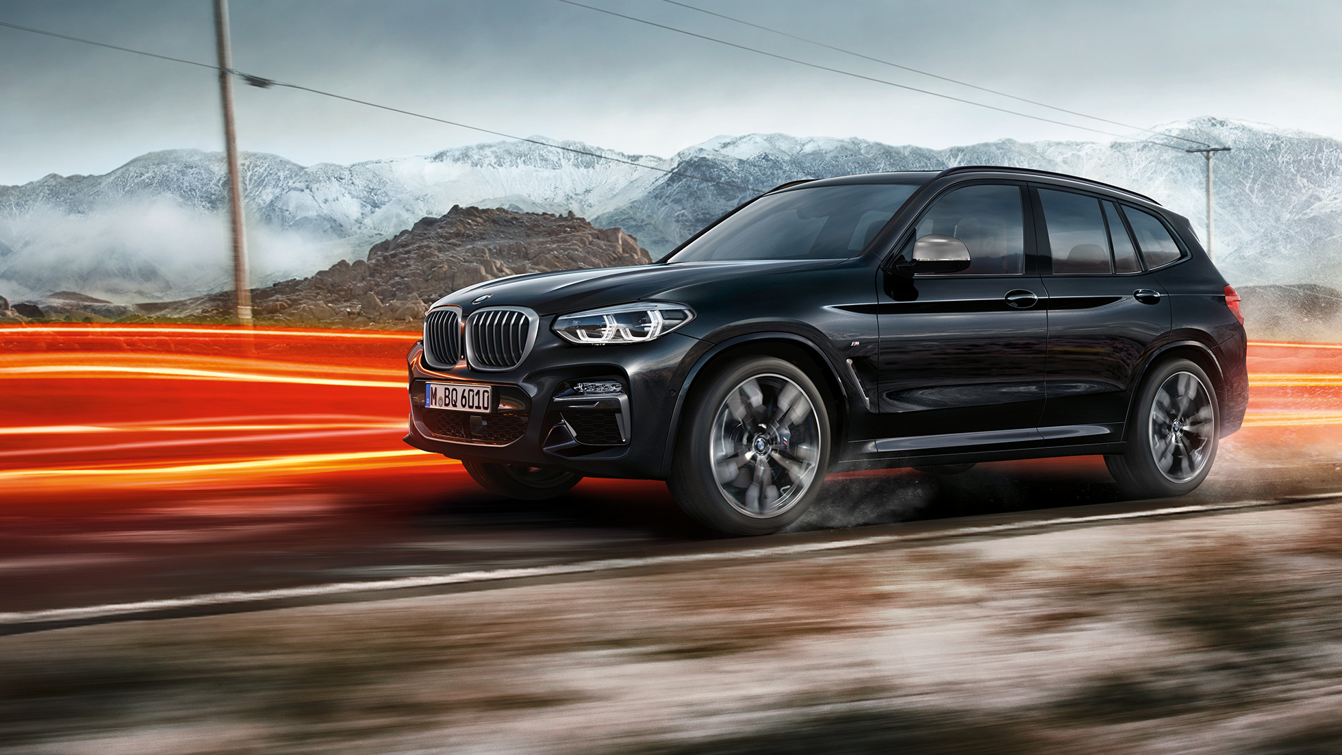 BMW X3 M40i und BMW X3 M40d, Seitenansicht. BMW X3 M40i und BMW X3 M40d in Saphirschwarz metallic, fahrend, Exterieur, Seitenansicht vor Berglandschaft mit Lichtstreifen.