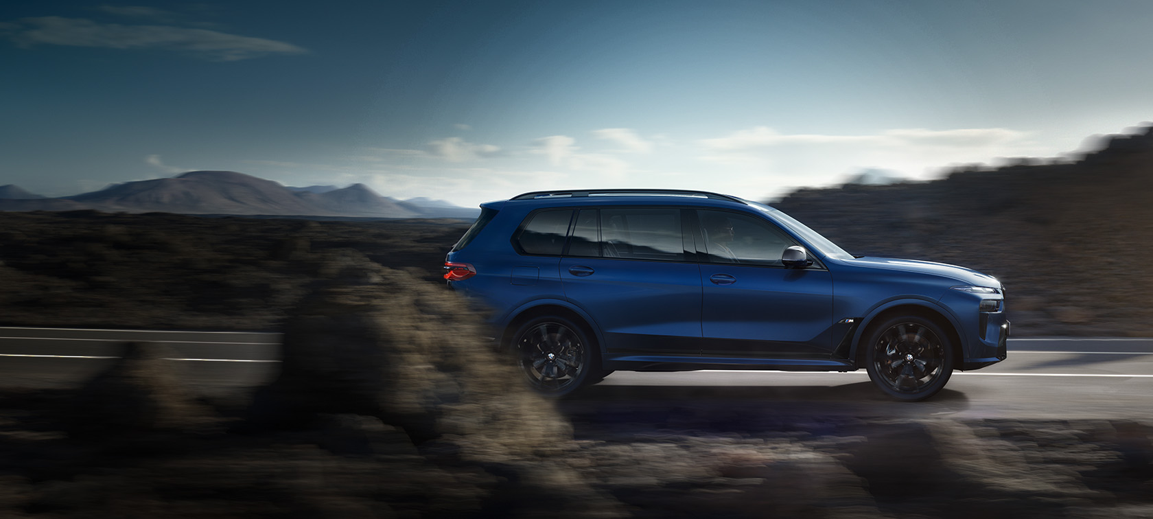 BMW X7 M60i xDrive G07 LCI Frozen Marina Bay Blue Seitenansicht fahrend auf der Straße vor Berglandschaft