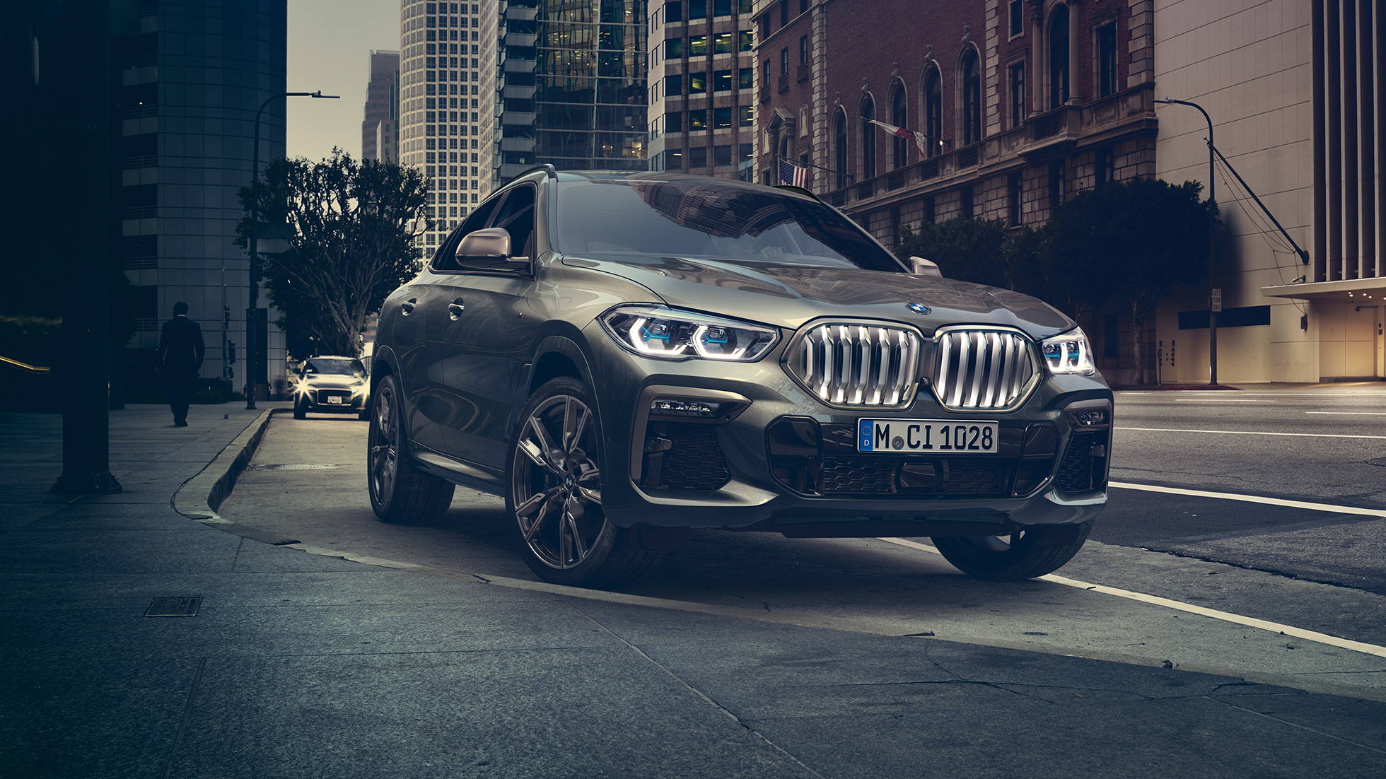 BMW X6 Adaptives M Fahrwerk Professional. BMW X6 in Dreiviertel-Front Perspektive vor urbaner Kulisse.