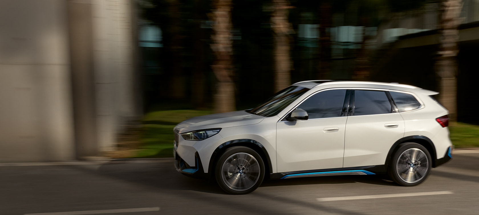 BMW iX1 U11 BEV 2022 Dreiviertel Seitenansicht BMW iX1 U11 BEV 2022 Mineralweiß metallic Dreiviertel Seitenansicht fahrend