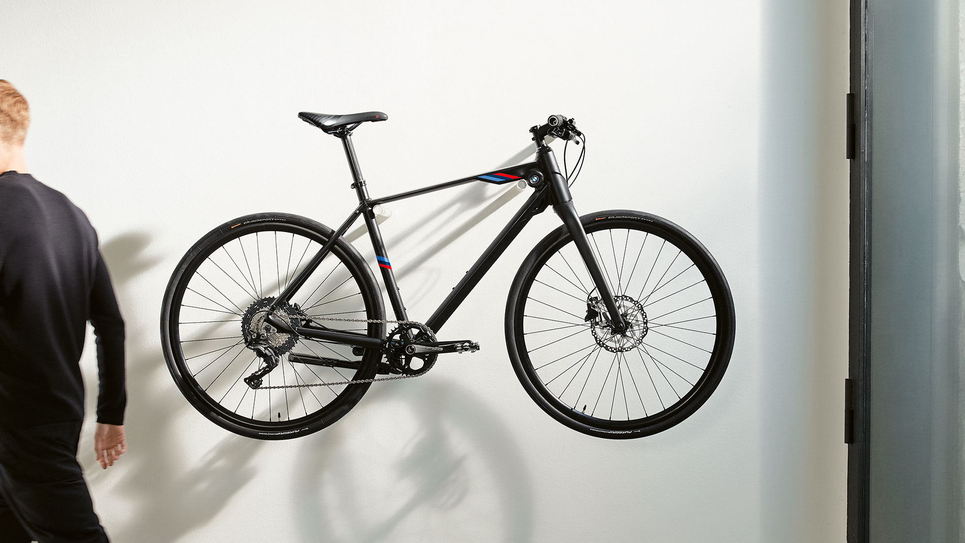 Das Bild zeigt das BMW M Bike Matt Black mit den BMW M Motorsport Streifen an einer Wandhalterung. Das Bild zeigt das BMW M Bike Matt Black mit den BMW M Motorsport Streifen an einer Wandhalterung.