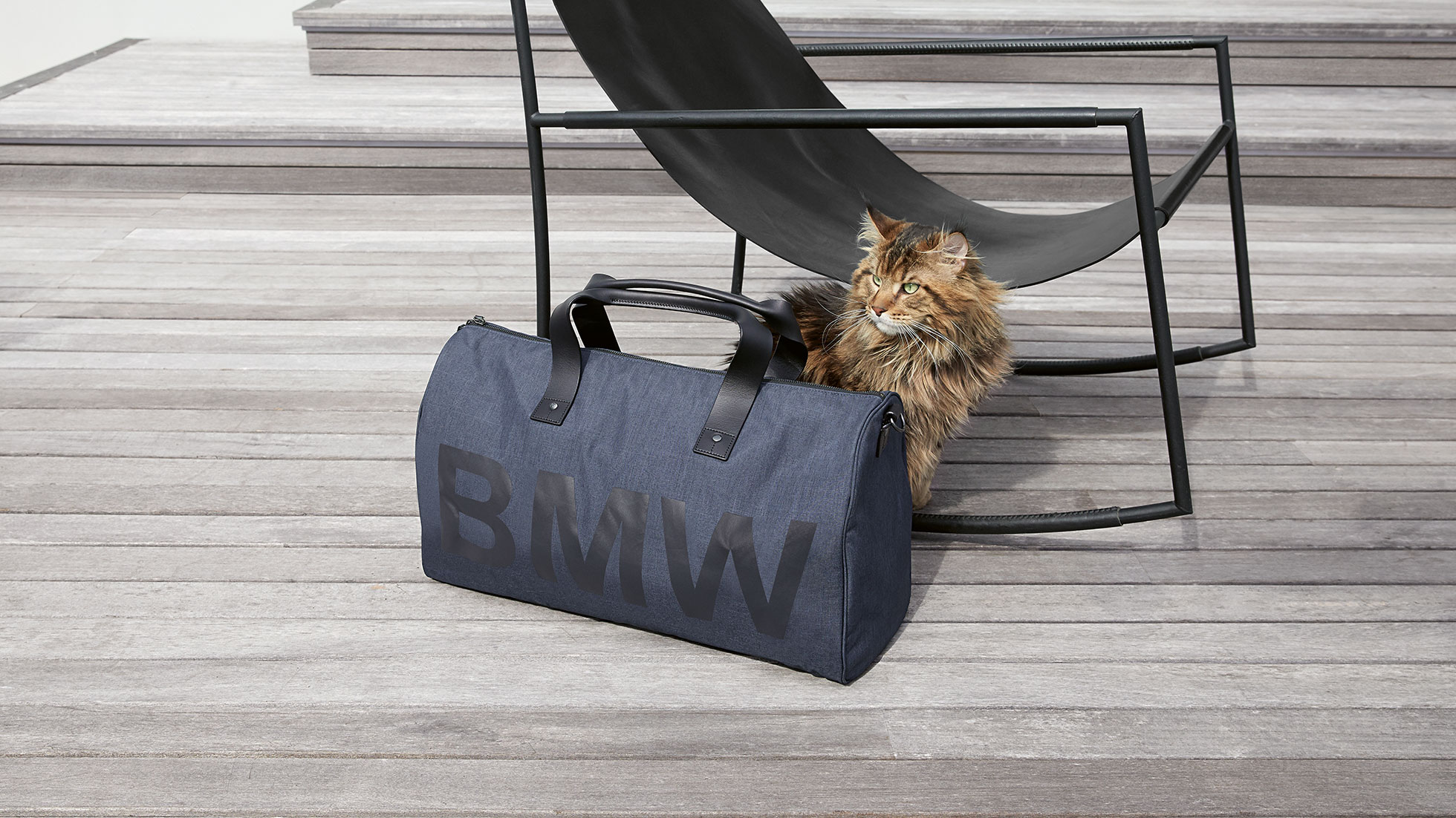 Auf dem Bild ist der BMW Modern Duffle Bag mit einer dahinter sitzenden Katze und Stuhl abgebildet. Auf dem Bild ist der BMW Modern Duffle Bag mit einer dahinter sitzenden Katze und Stuhl abgebildet.
