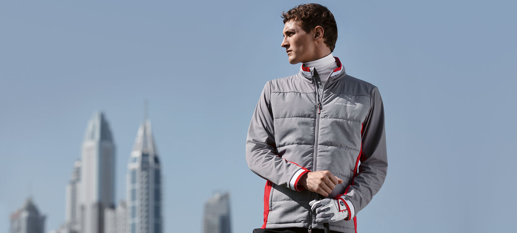 Auf dem Bild präsentiert ein Mann vor der Skyline einer Großstadt Kollektionsteile der BMW Golfsport Collection. Auf dem Bild präsentiert ein Mann vor der Skyline einer Großstadt Kollektionsteile der BMW Golfsport Collection.
