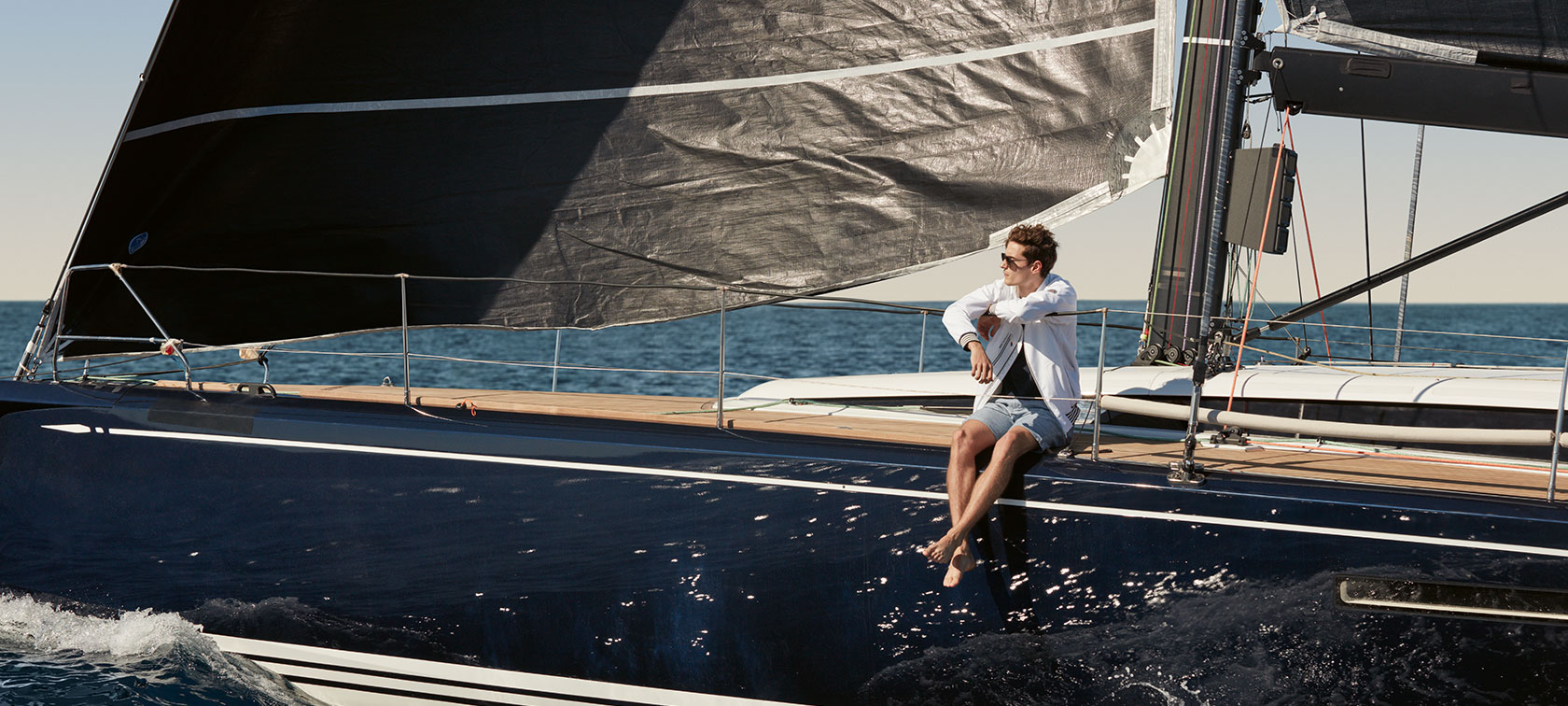 Auf dem Bild sehen Sie einen jungen Mann, der auf einem Segelschiff Kollektionsteile der BMW Yachtsport Collection präsentiert. Auf dem Bild sehen Sie einen jungen Mann, der auf einem Segelschiff Kollektionsteile der BMW Yachtsport Collection präsentiert.