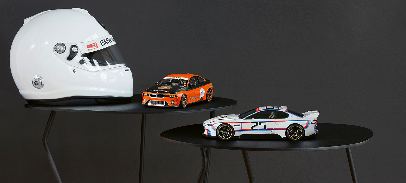 Auf dem Bild sind die Miniaturen BMW 2002 Hommage Turbomeister und BMW 3.0 CSL 25, rechts neben einem weißen Helm, platziert. Auf dem Bild sind die Miniaturen BMW 2002 Hommage Turbomeister und BMW 3.0 CSL 25, rechts neben einem weißen Helm, platziert.