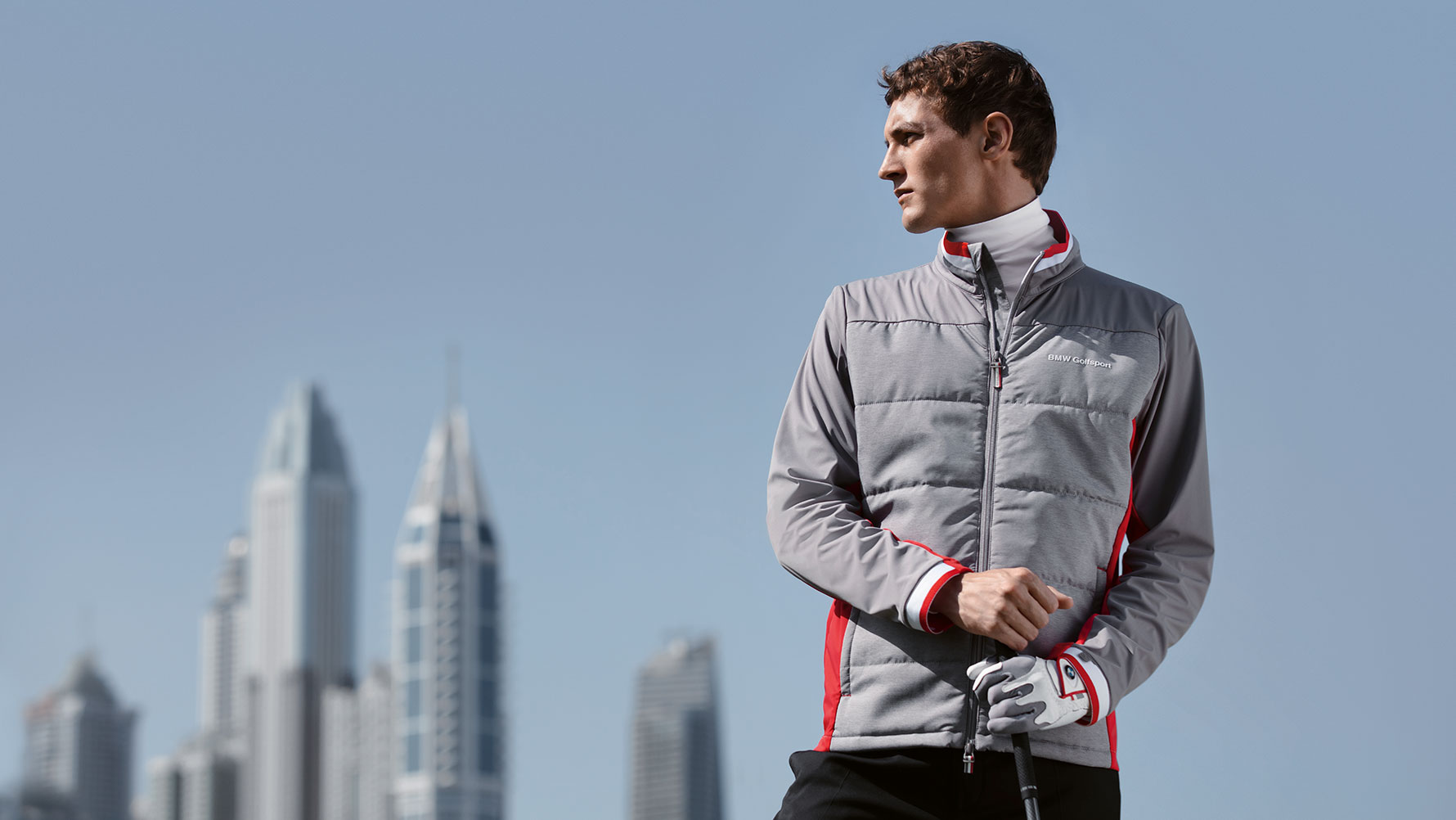Vor einer Skyline präsentiert ein männliches Model Produkte der BMW Golfsport Collection. Vor einer Skyline präsentiert ein männliches Model Produkte der BMW Golfsport Collection.