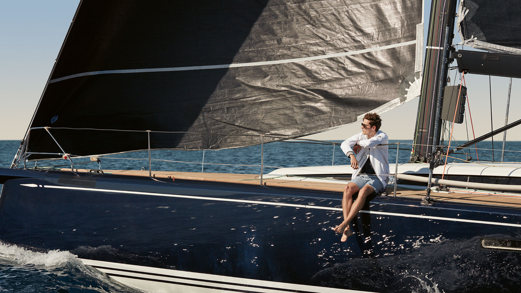 Ein Mann genießt den Fahrtwind auf einem Segelboot und zeigt dabei Bekleidung aus der BMW Yachtsport Collection. Ein Mann genießt den Fahrtwind auf einem Segelboot und zeigt dabei Bekleidung aus der BMW Yachtsport Collection.