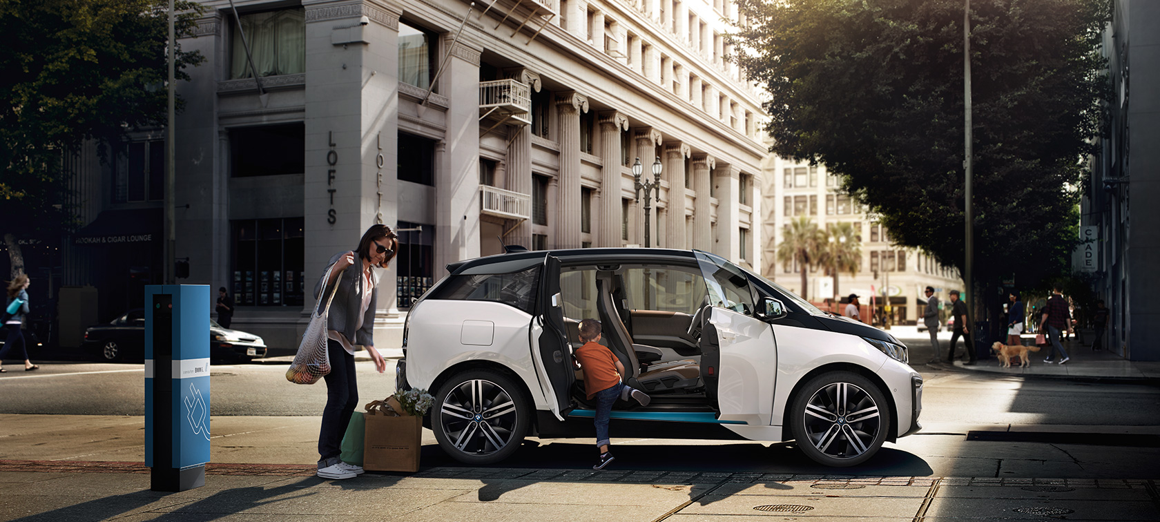 BMW i3 vor urbaner Kulisse BMW Reichweite - BMW i3 vor urbaner Kulisse mit Frau und Kind