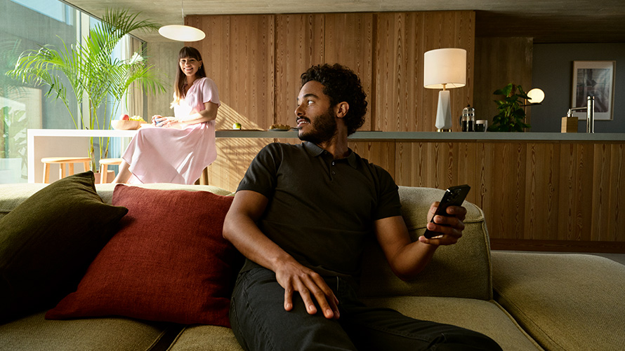 Teilen BMW Digital Key BMW Digital Key Teilen Mann mit Smartphone in der Hand sitzend auf dem Sofa mit Frau im Hintergrund