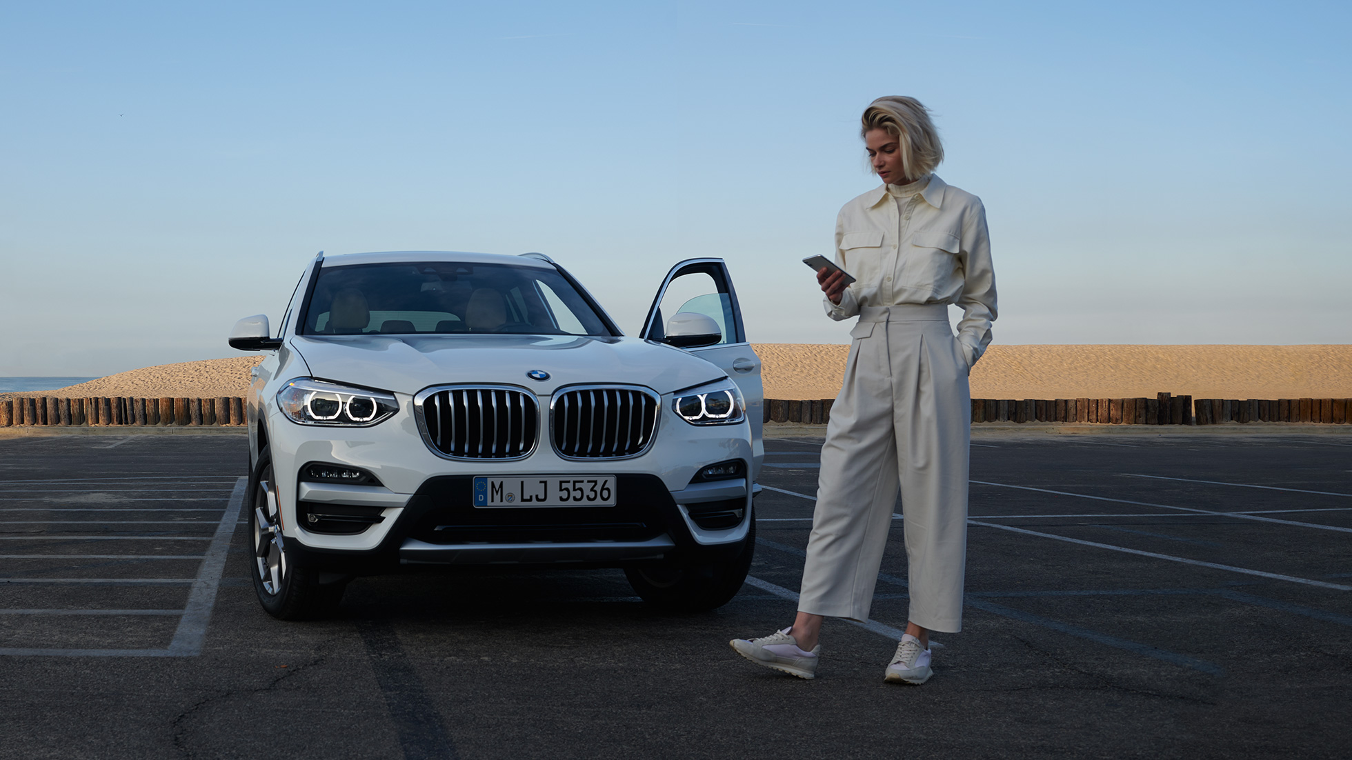 Frau benutzt My BMW App auf dem Smartphone Frau benutzt My BMW App von BMW ConnectedDrive auf dem Smartphone vor weißem BMW X5