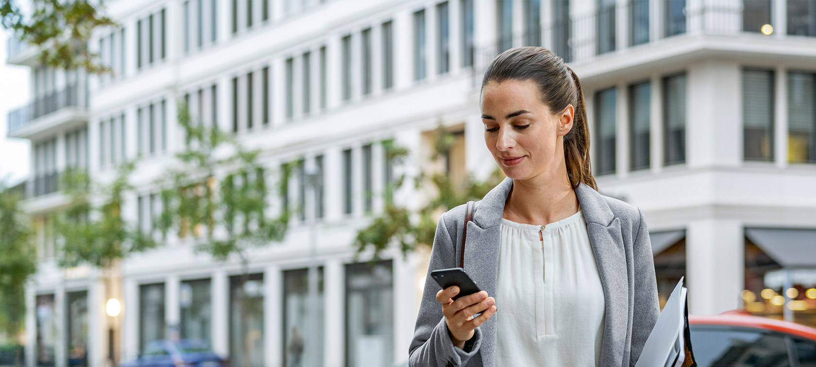 Frau steht vor Gebäude und schaut auf ihr Smartphone Remote Software Upgrade Frau steht vor Gebäude und schaut auf ihr Smartphone