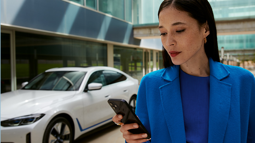 Frau stehend vor einem BMW Frau stehend vor einem BMW und schaut auf ihr Smartphone