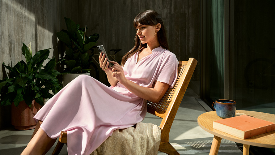 Frau im rosa Kleid mit Smartphone in der Hand Remote Inside View Remote Inside View Frau im rosa Kleid mit Smartphone in der Hand auf einem Stuhl
