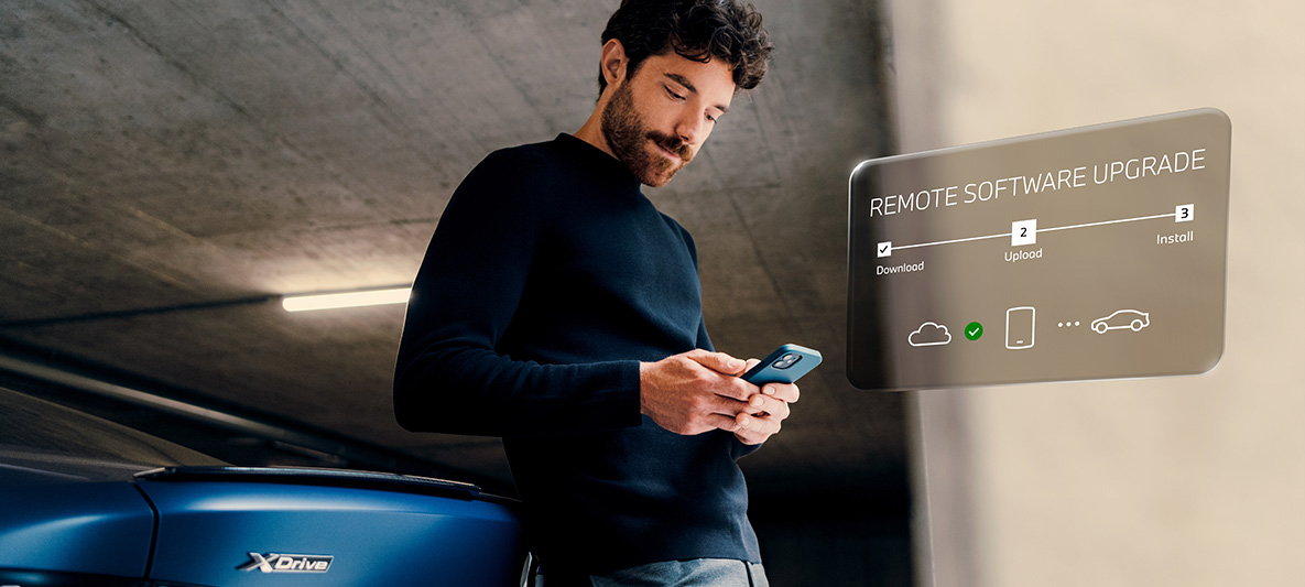 Mann lehnt an BMW Heck und schaut auf sein Smartphone Remote Software Upgrade Mann lehnt an BMW Heck und schaut auf sein Smartphone