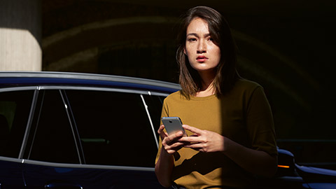 BMW ConnectedDrive Übersicht Frau mit Smartphone in den Händen mit BMW im Hintergrund