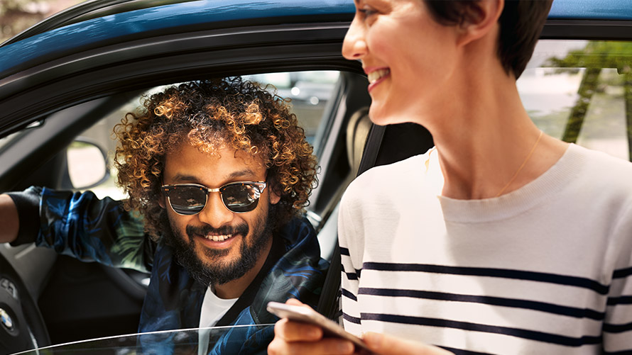 BMW Connected Mann im BMW und Frau außerhalb des BMW nutzen BMW Connected auf dem Smartphone