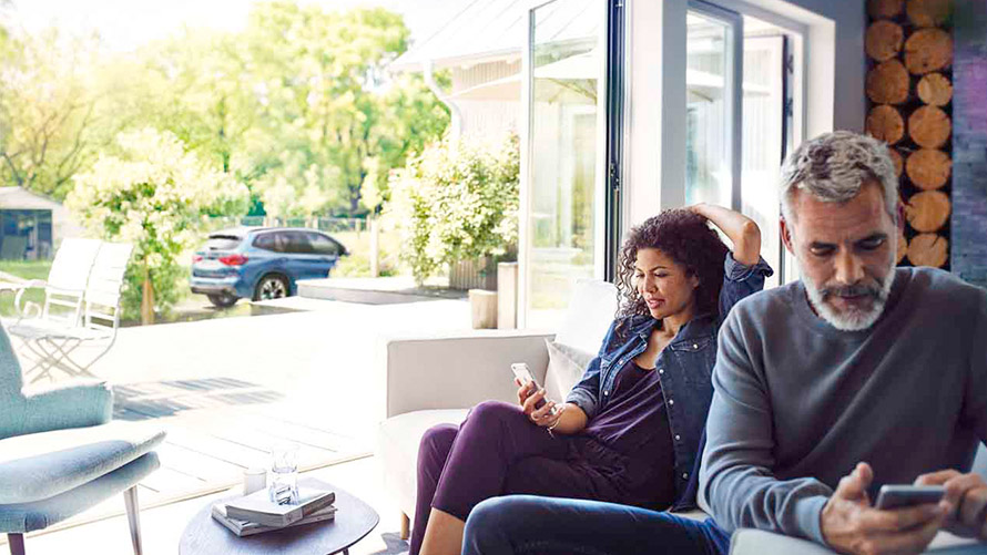 Remote Services Mann und Frau sitzen auf Sofa und nutzen Remote Services auf ihren Smartphones