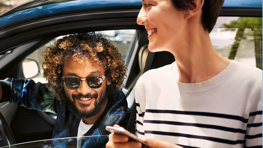 BMW Connected Mann im BMW und Frau außerhalb des BMW nutzen BMW Connected auf dem Smartphone