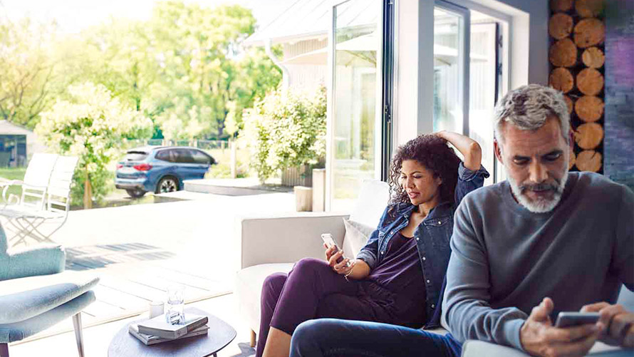 Remote Services Mann und Frau sitzen auf Sofa und nutzen Remote Services auf ihren Smartphones