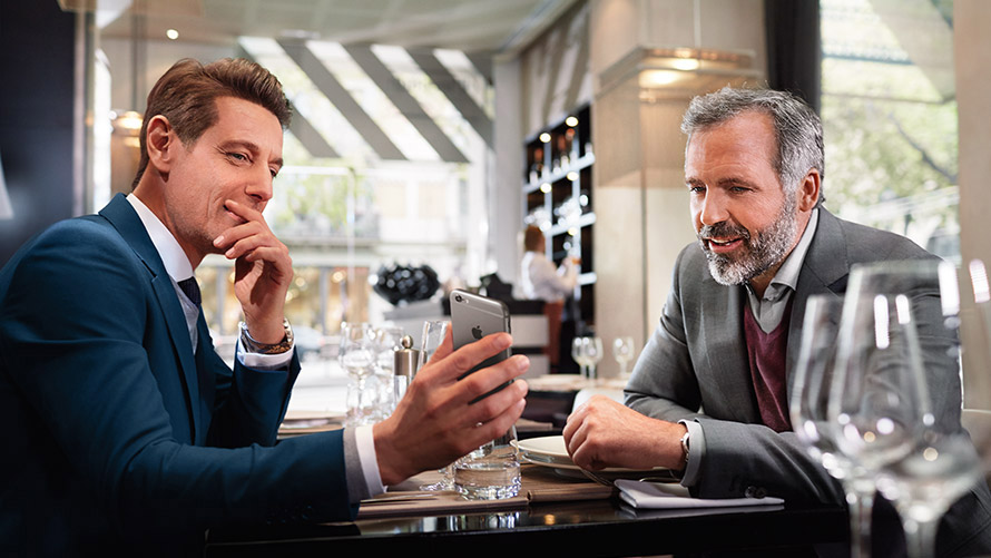 Verwalte deine Lieblingsziele Zwei Männer im Restaurant nutzen Funktion „Verwalte deine Lieblingsziele” auf Smartphone