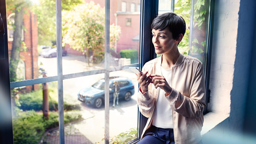 Share Live Trip Status Frau sitzt vor Fenster und nutzt Share Live Trip Status auf Smartphone