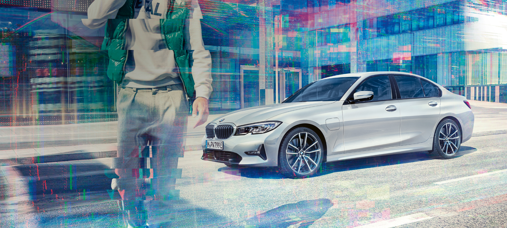 BMW 3er Limousine, Seitschuss BMW 330e. Dreiviertel-Seitschuss der stehenden BMW 330e Limousine vor urbanem Glasgebäude mit sich bewegenden Passanten.
