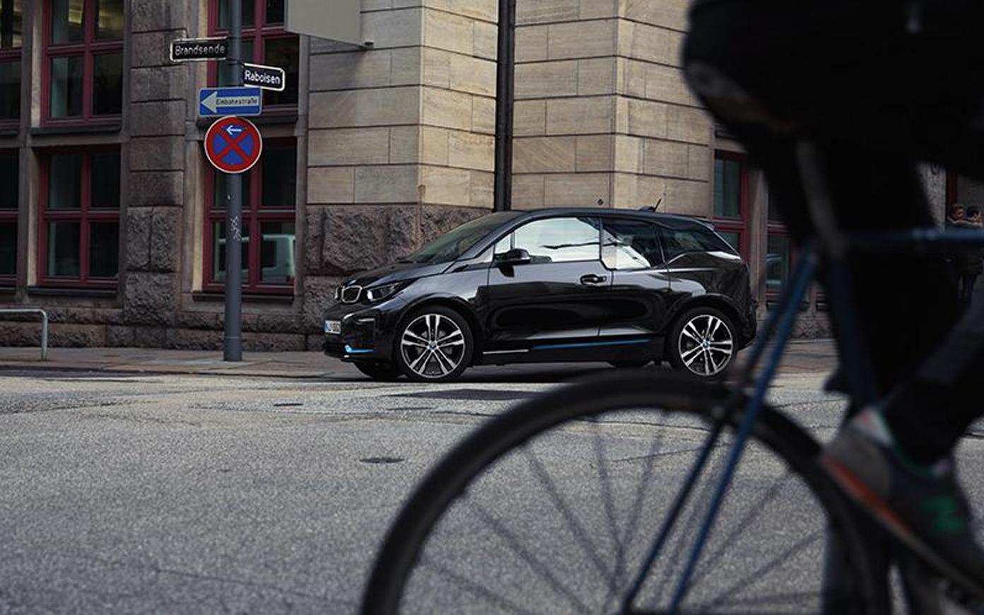 BMW i3s I01 2018 Fluid Black mit Akzent BMW i Blau Seitenansicht in urbaner Kulisse fahrend