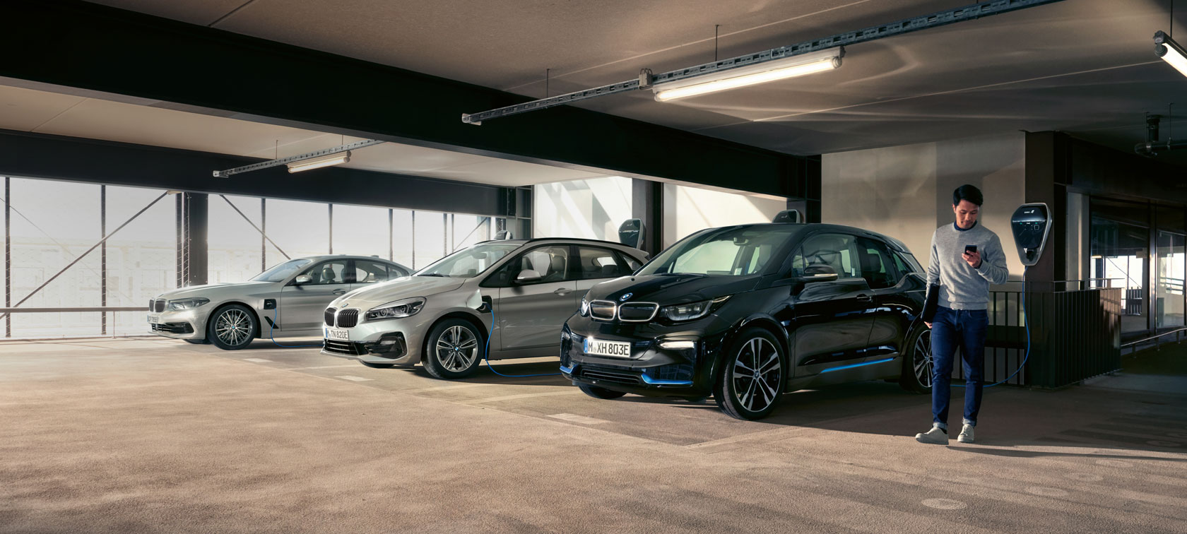 BMW i3s in Seitenansicht an der BMW i Wallbox vor natürlicher Kulisse.