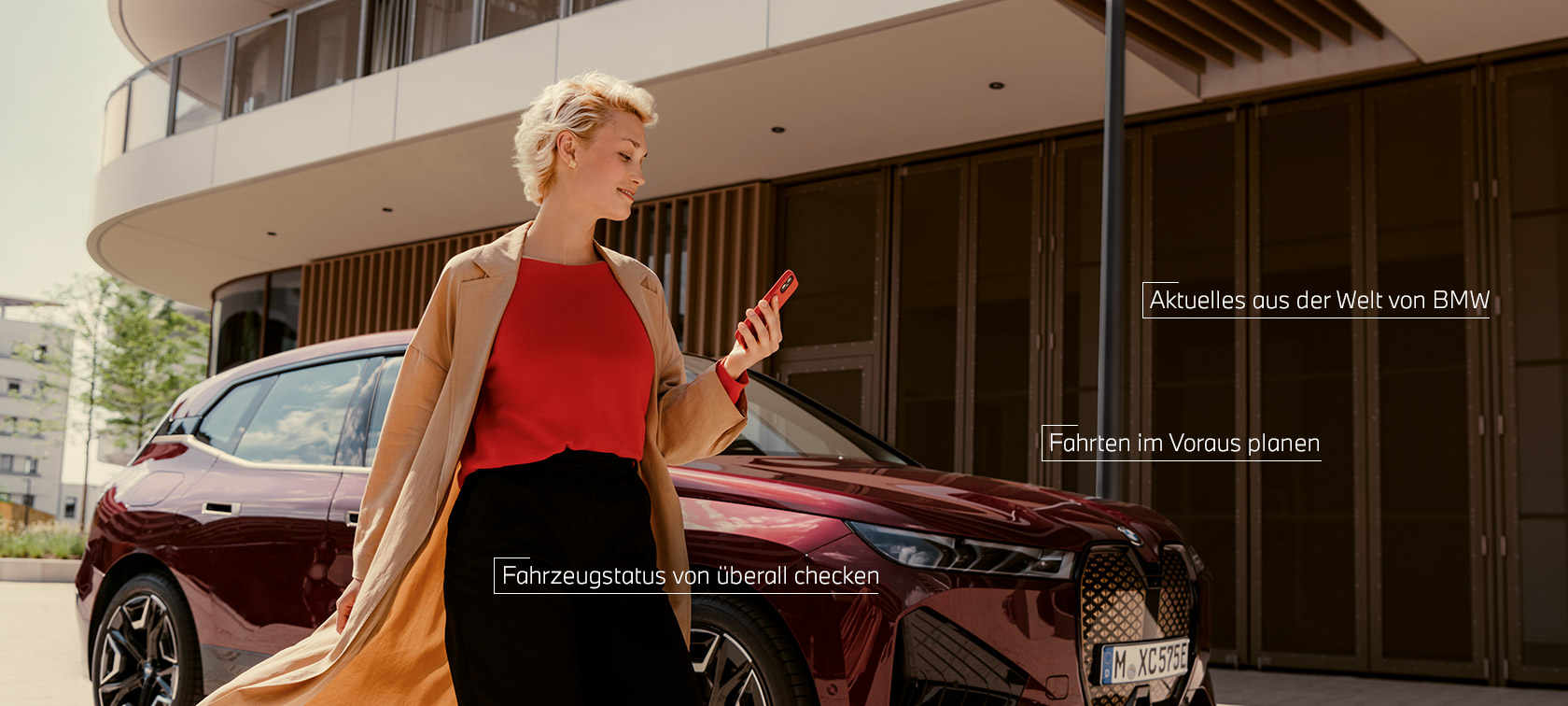 My BMW App Frau vor BMW iX und benutzt My BMW App auf Smartphone