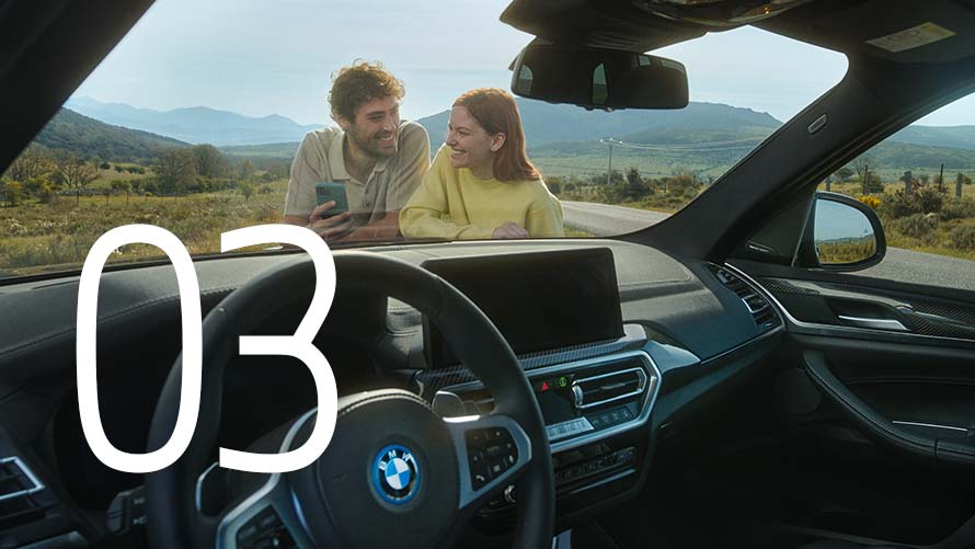 Eine Frau läuft lächelnd an einem BMW iX vorbei und schaut über ihre Schulter.